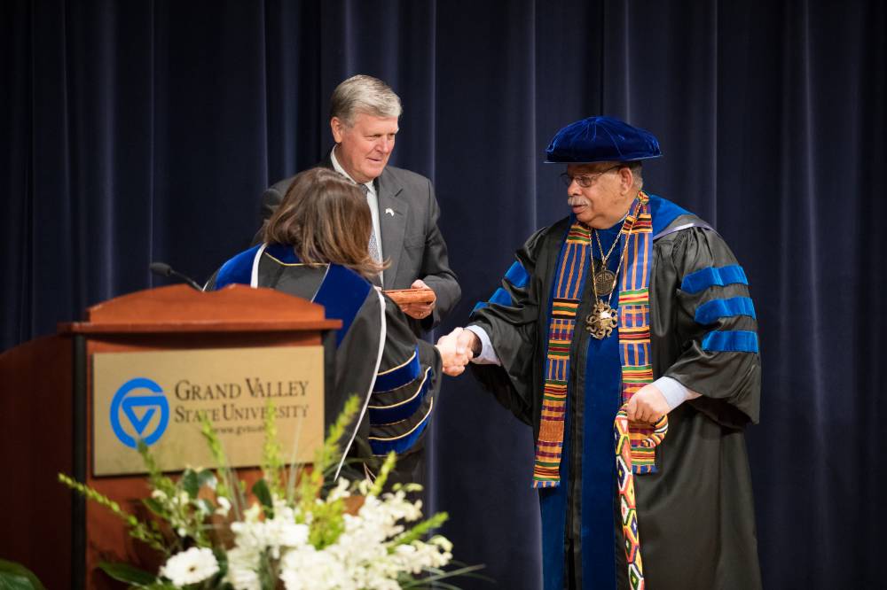 Provost Cimitile on stage with President Emeritus Haas and shaking hands with a  faculty member.